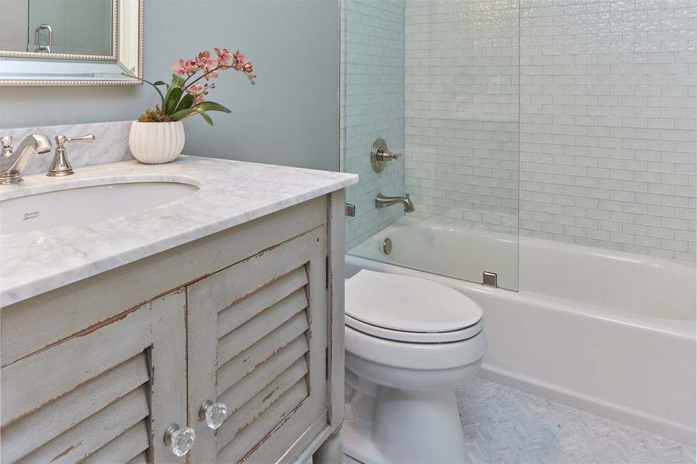 На фото: ванная комната среднего размера в стиле неоклассика (современная классика) с унитазом-моноблоком, синей плиткой, стеклянной плиткой, полом из керамогранита, душевой кабиной, врезной раковиной, белым полом, открытым душем, фасадами с филенкой типа жалюзи, искусственно-состаренными фасадами, ванной в нише, душем над ванной, столешницей из искусственного кварца и серыми стенами с
