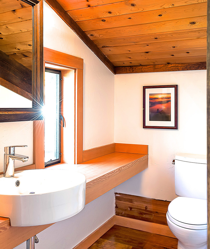 Ejemplo de cuarto de baño rural pequeño con lavabo sobreencimera, encimera de madera, sanitario de una pieza, paredes blancas, suelo de madera en tonos medios y aseo y ducha