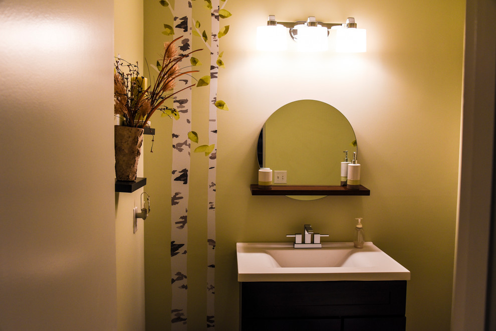 Maritim inredning av ett litet badrum, med möbel-liknande, skåp i mörkt trä, en toalettstol med separat cisternkåpa, gröna väggar, klinkergolv i porslin, ett nedsänkt handfat, bänkskiva i akrylsten och brunt golv