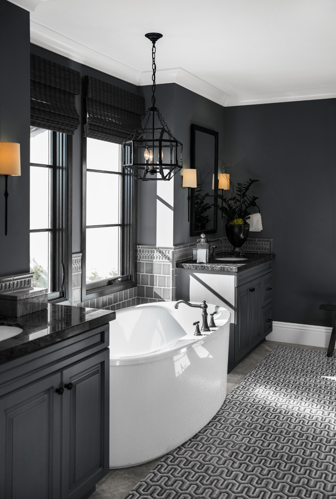 Example of a transitional 3/4 gray tile gray floor freestanding bathtub design in San Diego with raised-panel cabinets, black cabinets, black walls, an undermount sink and black countertops