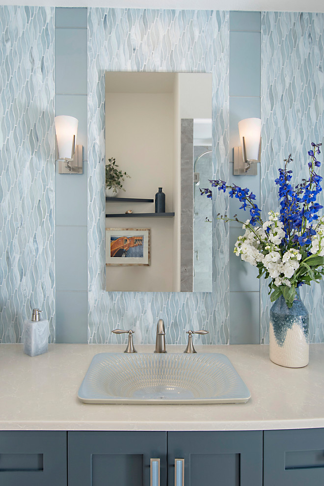 Cette image montre une salle de bain traditionnelle de taille moyenne avec un placard à porte shaker, des portes de placard bleues, WC à poser, un carrelage bleu, un carrelage en pâte de verre, un mur blanc, un sol en carrelage de porcelaine, un lavabo posé, un plan de toilette en quartz modifié, un sol beige, une cabine de douche à porte battante et un plan de toilette blanc.