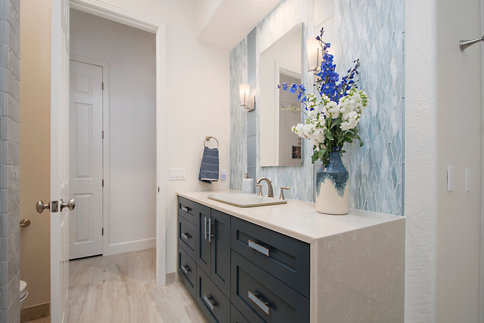 Design ideas for a medium sized traditional shower room bathroom in San Diego with shaker cabinets, blue cabinets, an alcove shower, a one-piece toilet, blue tiles, glass tiles, white walls, porcelain flooring, a built-in sink, engineered stone worktops, a hinged door and white worktops.