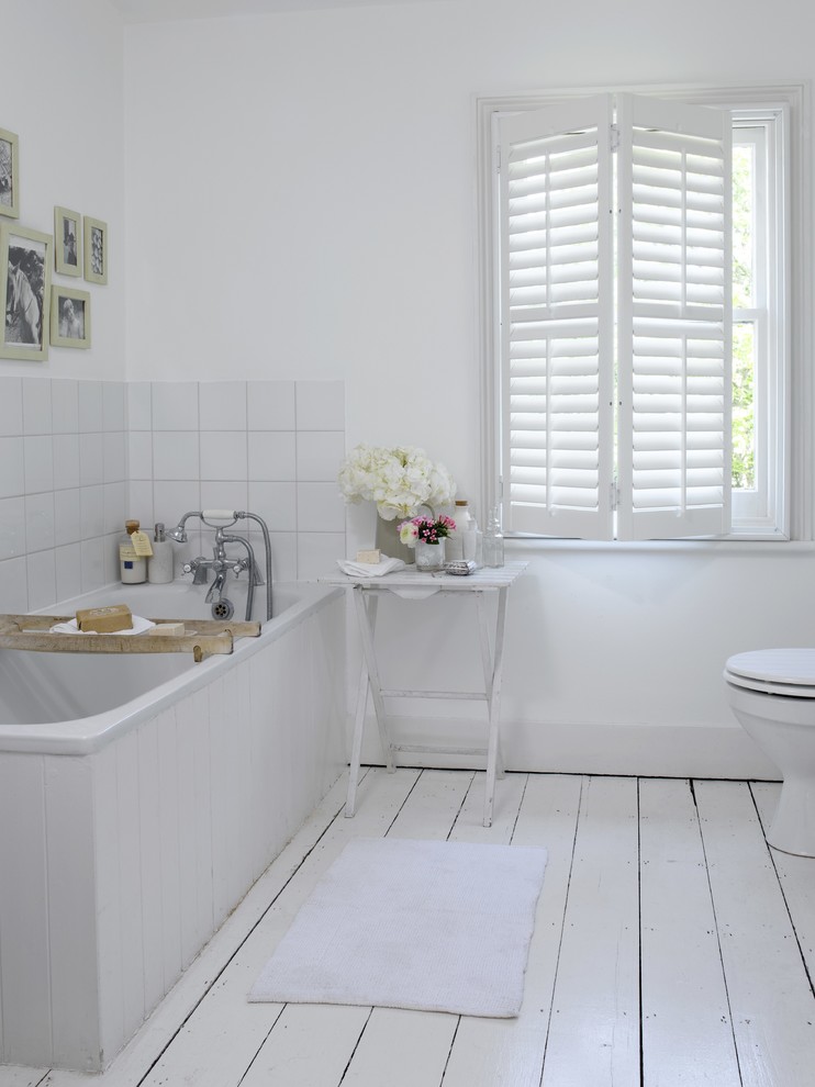 Cette photo montre une salle de bain nature avec une baignoire d'angle, un carrelage blanc, un mur blanc, parquet peint et un sol blanc.