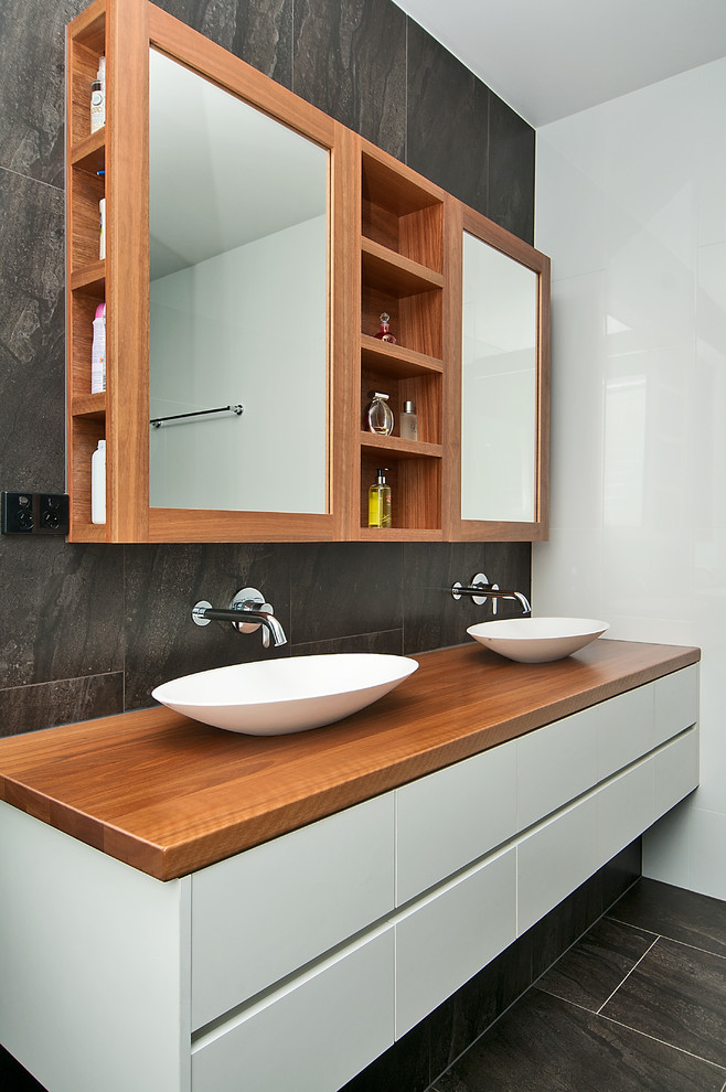 Cette photo montre une grande salle de bain principale moderne en bois brun avec une vasque, un plan de toilette en bois, un carrelage gris, un mur multicolore et un placard à porte plane.