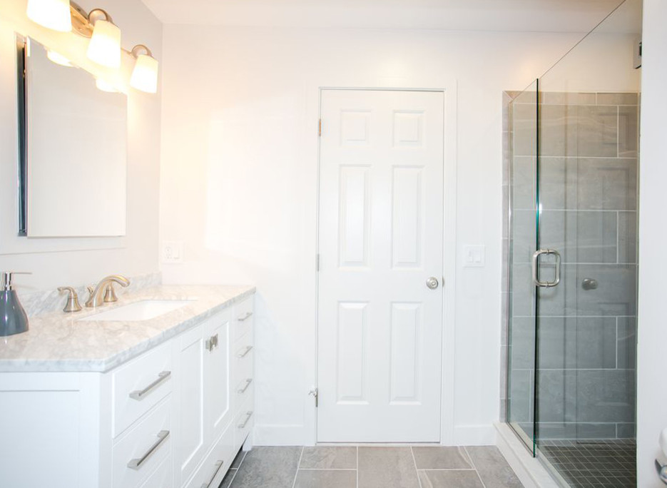 Bild på ett litet maritimt grå grått badrum, med vita skåp, en dusch i en alkov, grå kakel, vita väggar, ett integrerad handfat, bänkskiva i kvarts, grått golv och dusch med gångjärnsdörr