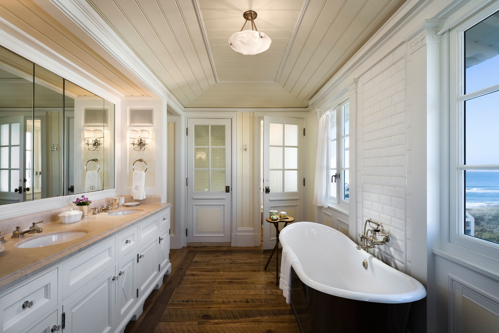 Idées déco pour une salle de bain bord de mer avec un lavabo encastré, un placard avec porte à panneau encastré, des portes de placard blanches, une baignoire indépendante, un carrelage blanc, un carrelage métro, un mur jaune et parquet foncé.