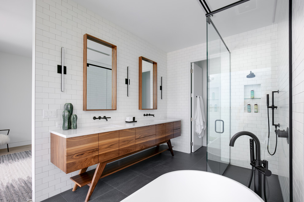 Photo of a medium sized contemporary ensuite bathroom in Other with freestanding cabinets, medium wood cabinets, a freestanding bath, a built-in shower, a two-piece toilet, white tiles, metro tiles, white walls, porcelain flooring, a submerged sink, engineered stone worktops, a hinged door, white worktops, grey floors, an enclosed toilet, double sinks and a freestanding vanity unit.