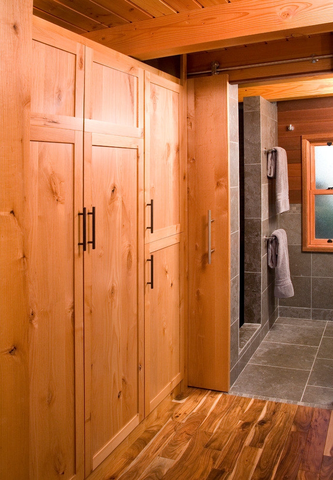 Rustik inredning av ett litet badrum med dusch, med grå kakel, stenkakel, skåp i mellenmörkt trä, en öppen dusch, en toalettstol med hel cisternkåpa, kalkstensgolv, ett piedestal handfat och släta luckor