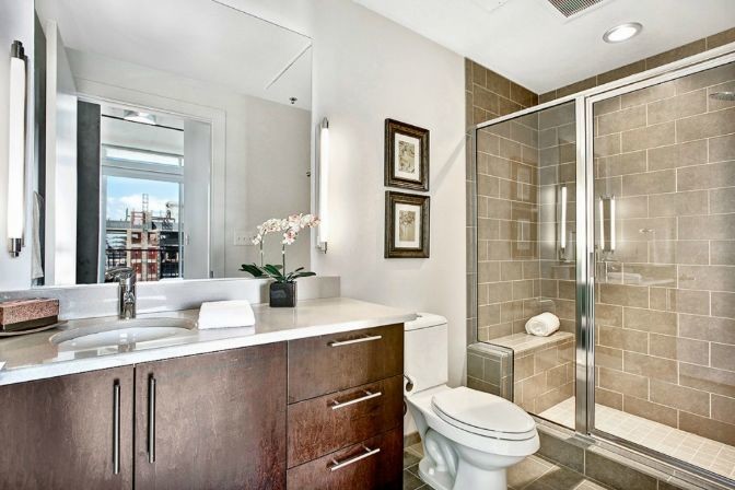 Example of a mid-sized trendy brown tile and stone tile corner shower design in Seattle with flat-panel cabinets, dark wood cabinets, a two-piece toilet, white walls, an undermount sink and quartz countertops