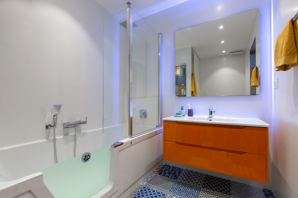 Идея дизайна: ванная комната в современном стиле с плоскими фасадами, оранжевыми фасадами, ванной в нише, душем над ванной, белой плиткой, белыми стенами, душевой кабиной, монолитной раковиной, разноцветным полом и белой столешницей