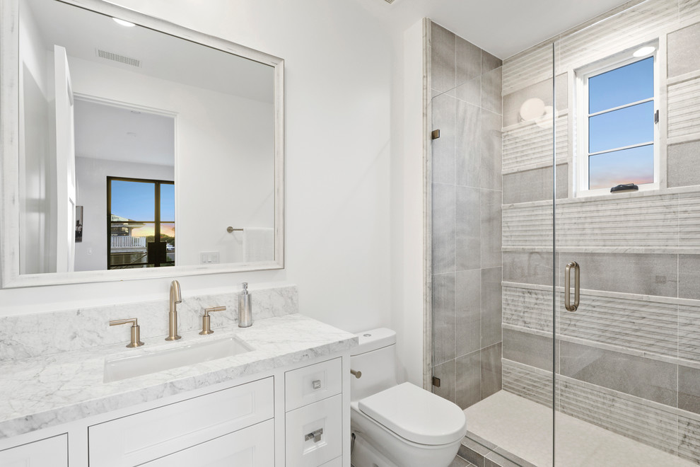 Свежая идея для дизайна: ванная комната в стиле модернизм с фасадами с утопленной филенкой, белыми фасадами, унитазом-моноблоком, серой плиткой, мраморной плиткой, белыми стенами, накладной раковиной, мраморной столешницей, серым полом, душем с распашными дверями, угловым душем и полом из керамической плитки - отличное фото интерьера