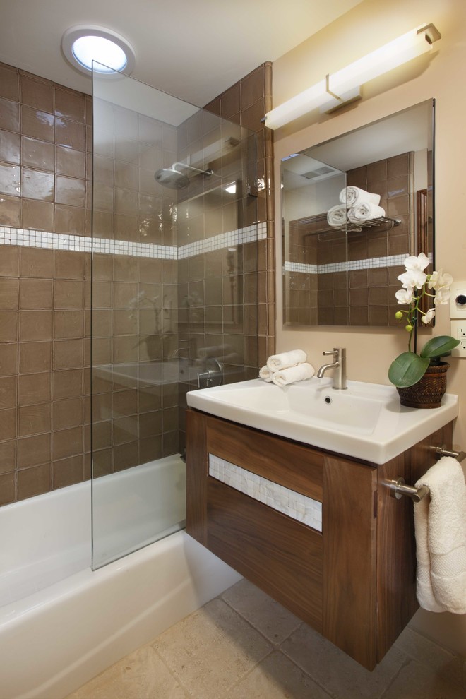 Идея дизайна: ванная комната в современном стиле с монолитной раковиной, плоскими фасадами, фасадами цвета дерева среднего тона, ванной в нише, душем над ванной и коричневой плиткой