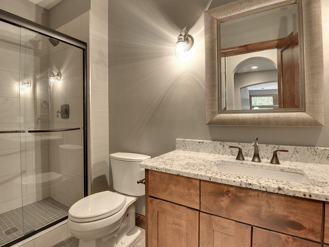 Klassisk inredning av ett stort badrum med dusch, med ett undermonterad handfat, luckor med infälld panel, skåp i mellenmörkt trä, marmorbänkskiva, en hörndusch, en toalettstol med hel cisternkåpa, vit kakel, porslinskakel, grå väggar och klinkergolv i porslin