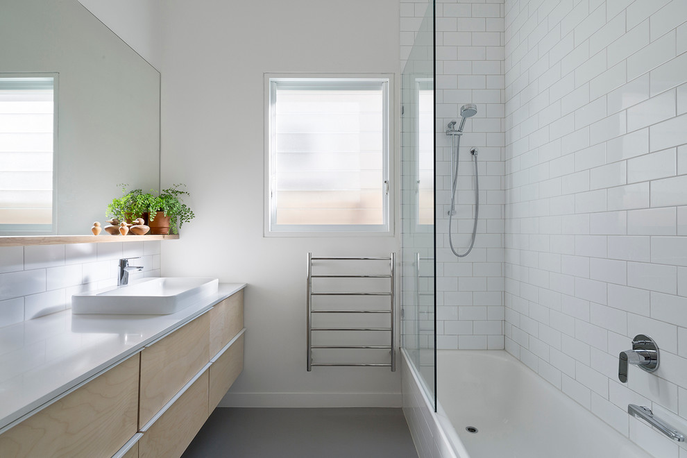 Inspiration for a small scandinavian bathroom in Melbourne with light wood cabinets, a shower/bath combination, a two-piece toilet, white tiles, metro tiles, white walls, lino flooring, quartz worktops, a built-in sink and an alcove bath.