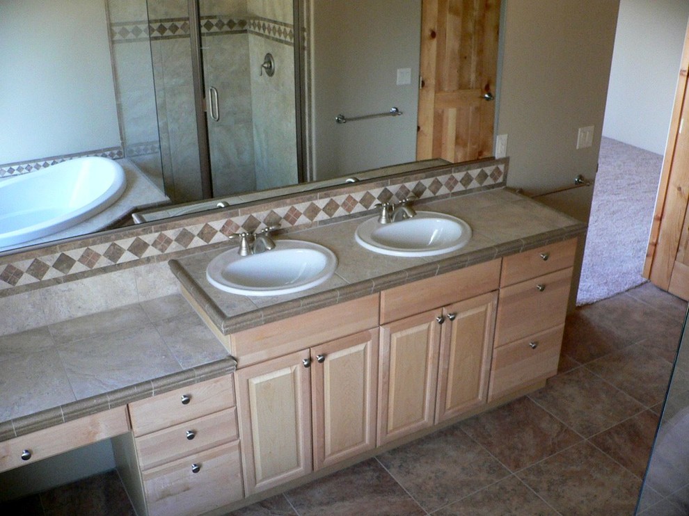 Cette photo montre une salle de bain chic en bois clair de taille moyenne avec un placard avec porte à panneau surélevé, une baignoire posée, une douche d'angle, un carrelage gris, des carreaux de porcelaine, un mur gris, un sol en carrelage de porcelaine, un plan de toilette en carrelage et un lavabo posé.