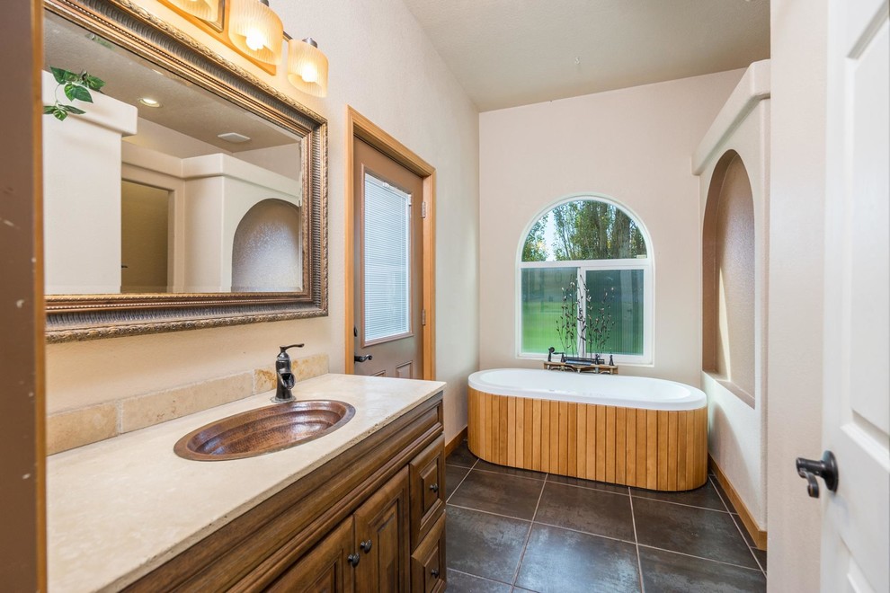 Réalisation d'une grande salle de bain tradition en bois foncé avec un placard avec porte à panneau surélevé, une baignoire indépendante, un mur beige et un lavabo posé.