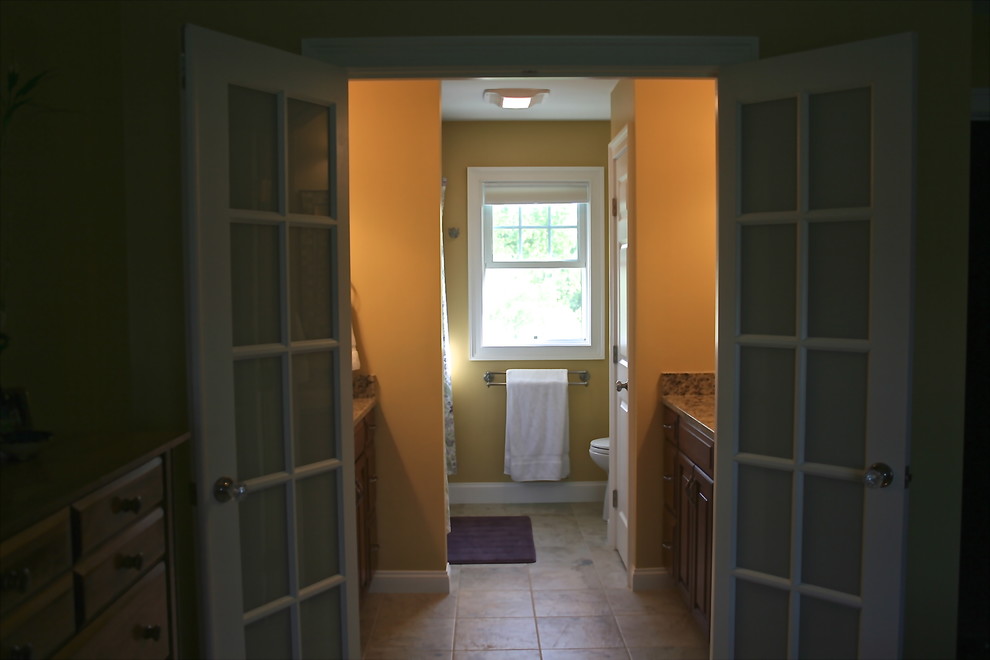 На фото: большая главная ванная комната в классическом стиле с фасадами с выступающей филенкой, темными деревянными фасадами, столешницей из гранита, бежевой плиткой, керамической плиткой, ванной в нише, душем над ванной, раздельным унитазом, врезной раковиной, желтыми стенами и полом из керамической плитки