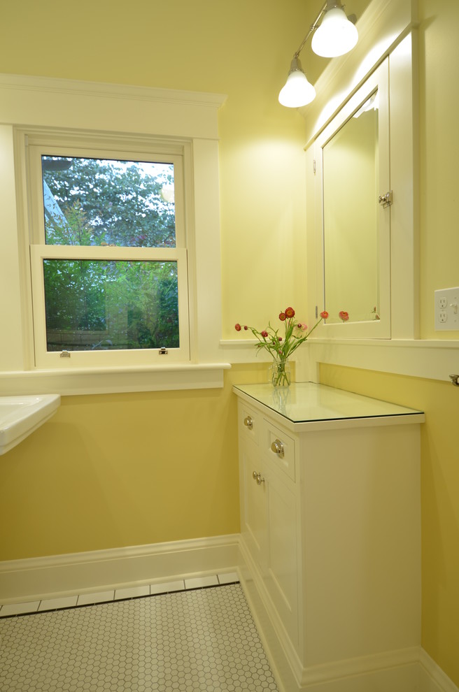 Bild på ett litet amerikanskt badrum, med luckor med profilerade fronter, vita skåp, vit kakel, keramikplattor, gula väggar, klinkergolv i keramik, ett piedestal handfat och bänkskiva i glas