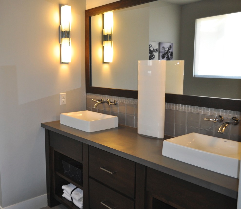 Cette photo montre une salle de bain principale chic en bois foncé de taille moyenne avec une vasque, un placard sans porte, un plan de toilette en surface solide, un carrelage gris, un carrelage en pâte de verre, un mur gris et un sol en carrelage de céramique.