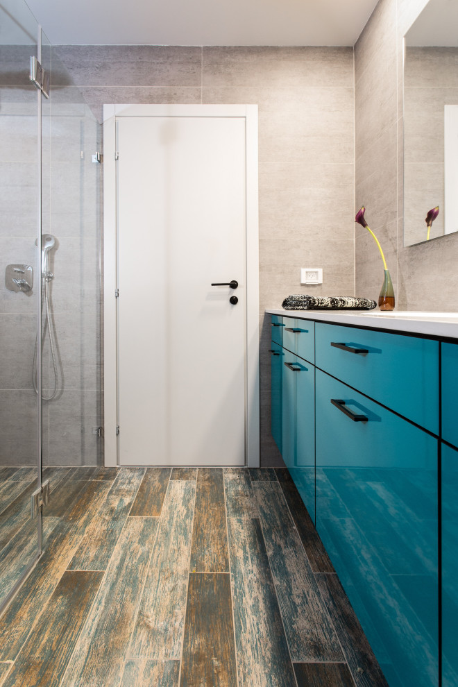 Inspiration för små moderna grönt badrum med dusch, med släta luckor, turkosa skåp, en kantlös dusch, en vägghängd toalettstol, grå kakel, porslinskakel, grå väggar, klinkergolv i porslin, ett konsol handfat, bänkskiva i akrylsten, turkost golv och dusch med gångjärnsdörr