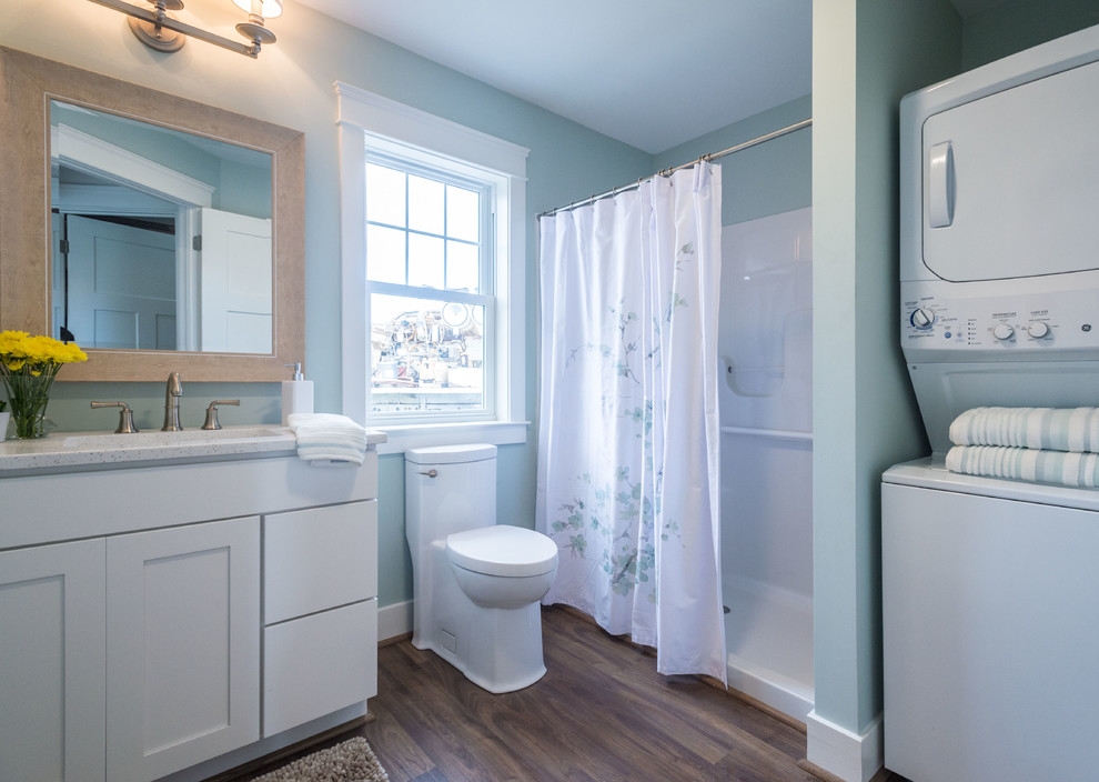 Cette photo montre une salle de bain chic avec un placard à porte shaker, des portes de placard blanches, une douche ouverte, WC à poser, un carrelage blanc, un mur bleu, sol en stratifié, un lavabo encastré, un plan de toilette en quartz, un sol marron, une cabine de douche avec un rideau et buanderie.