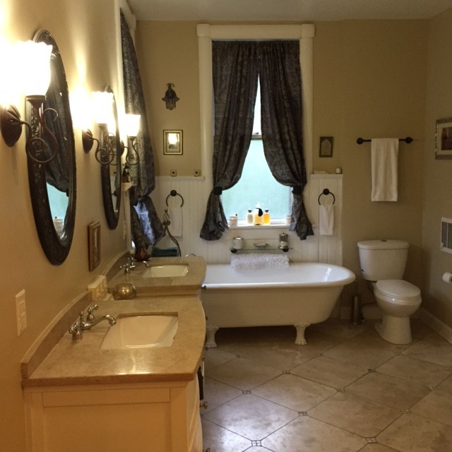 Inspiration for a large victorian master beige tile and stone tile travertine floor claw-foot bathtub remodel in Indianapolis with an undermount sink, shaker cabinets, beige cabinets, solid surface countertops and beige walls
