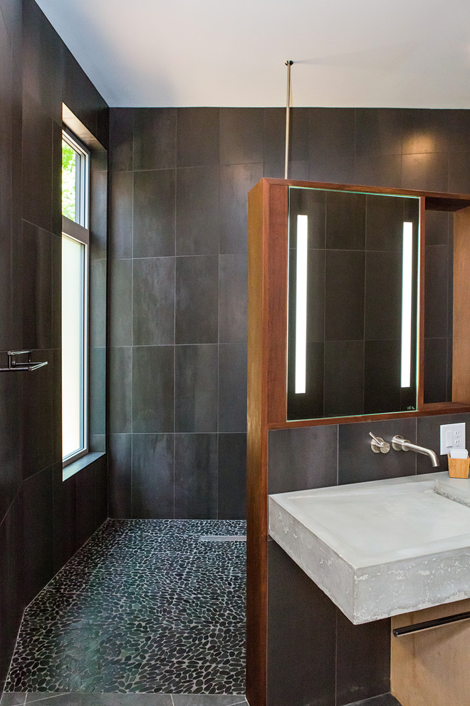 Modern inredning av ett stort grå grått en-suite badrum, med släta luckor, skåp i ljust trä, en öppen dusch, en vägghängd toalettstol, svart kakel, porslinskakel, svarta väggar, betonggolv, ett avlångt handfat, bänkskiva i betong, grått golv och med dusch som är öppen
