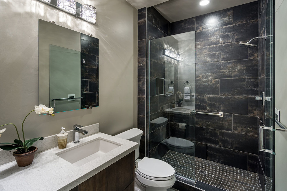 Modern inredning av ett mellanstort badrum med dusch, med ett undermonterad handfat, släta luckor, skåp i mörkt trä, bänkskiva i kvarts, en dusch i en alkov, en toalettstol med separat cisternkåpa, svart kakel, porslinskakel, grå väggar och klinkergolv i porslin
