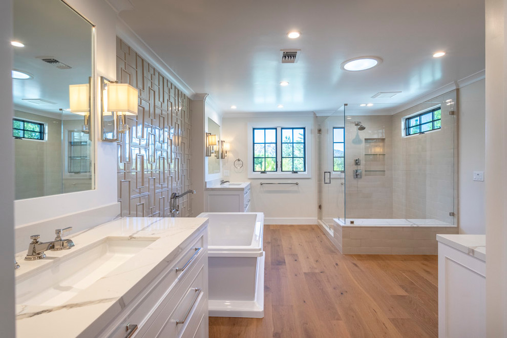 Exemple d'une très grande salle de bain principale chic avec un placard avec porte à panneau encastré, des portes de placard blanches, une baignoire indépendante, un carrelage beige, un mur blanc, un sol en bois brun, un plan de toilette en quartz modifié et un plan de toilette blanc.