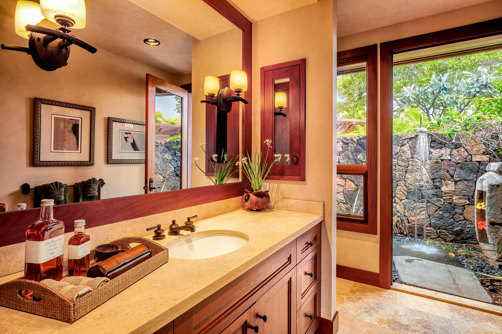 Photo of a medium sized world-inspired ensuite bathroom in Hawaii with a built-in sink, raised-panel cabinets, medium wood cabinets, solid surface worktops, a two-piece toilet, beige tiles, stone tiles, beige walls and travertine flooring.