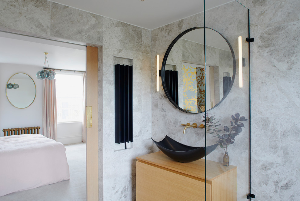 На фото: главная ванная комната среднего размера в стиле модернизм с фасадами островного типа, светлыми деревянными фасадами, отдельно стоящей ванной, душевой комнатой, инсталляцией, серой плиткой, плиткой из известняка, серыми стенами, полом из известняка, настольной раковиной, столешницей из дерева, серым полом, открытым душем и бежевой столешницей с