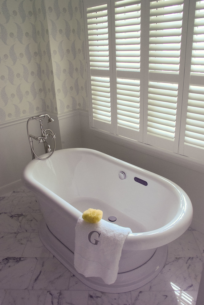 Inredning av ett klassiskt en-suite badrum, med ett undermonterad handfat, släta luckor, vita skåp, marmorbänkskiva, ett fristående badkar, en dusch i en alkov, en toalettstol med separat cisternkåpa, vit kakel, stenkakel och marmorgolv