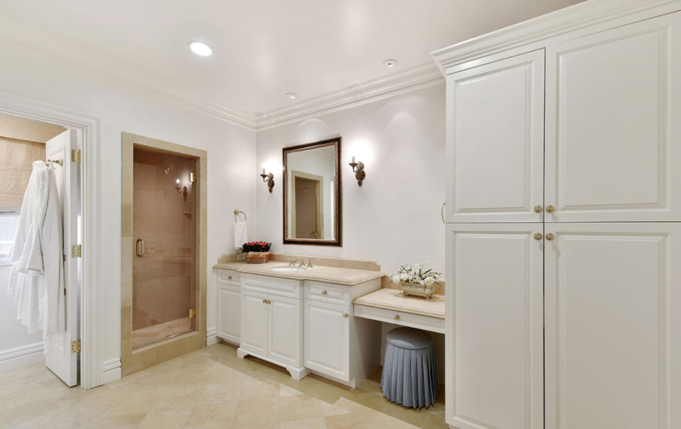 Aménagement d'une grande salle de bain classique avec un placard avec porte à panneau surélevé, des portes de placard blanches, une baignoire posée, un carrelage beige, du carrelage en travertin, un mur blanc, un sol en calcaire, un lavabo encastré, un plan de toilette en calcaire, un sol beige et une cabine de douche à porte battante.