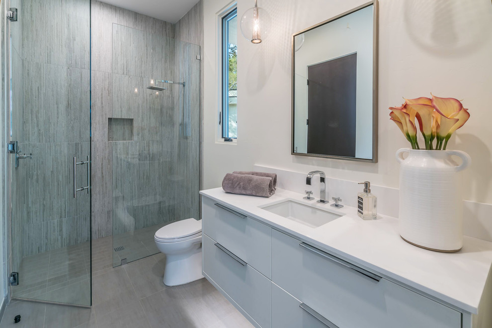 This is an example of a large contemporary ensuite bathroom in Santa Barbara with flat-panel cabinets, medium wood cabinets, a freestanding bath, a built-in shower, white walls, porcelain flooring, a submerged sink, marble worktops, grey floors, a hinged door and multi-coloured worktops.