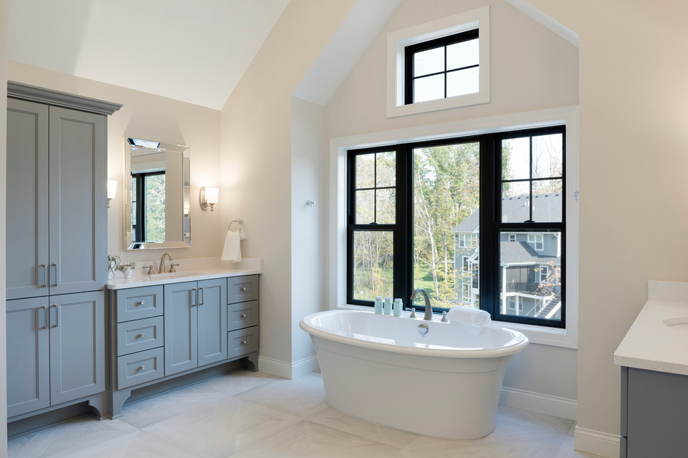 Foto de cuarto de baño clásico con armarios estilo shaker, puertas de armario grises, bañera exenta, paredes blancas, lavabo bajoencimera, suelo blanco y encimeras blancas