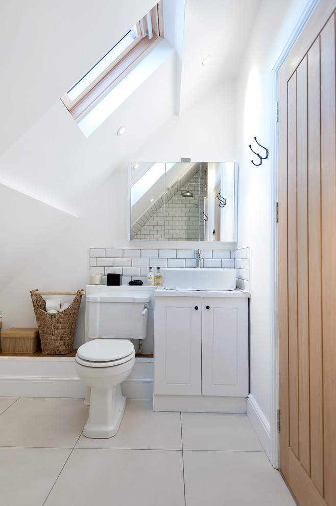 Modelo de cuarto de baño de estilo de casa de campo con lavabo sobreencimera, puertas de armario blancas, sanitario de dos piezas, baldosas y/o azulejos blancos, baldosas y/o azulejos de cemento y paredes blancas