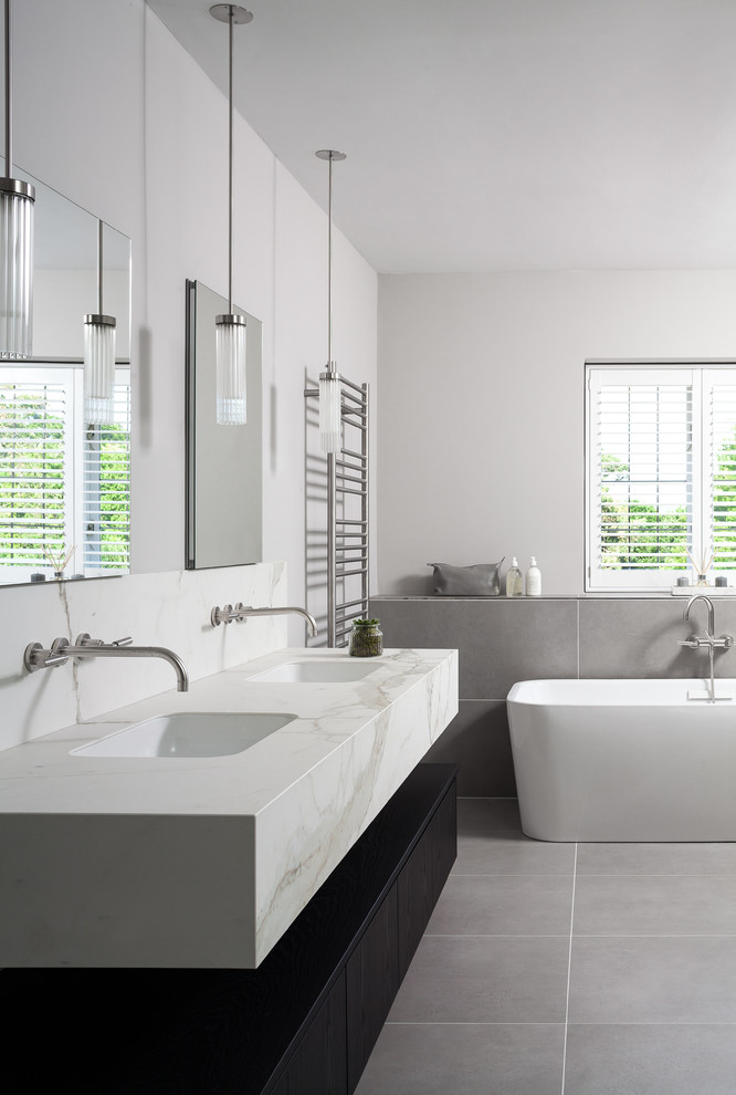 Пример оригинального дизайна: главная ванная комната среднего размера в современном стиле с отдельно стоящей ванной, серой плиткой, белыми стенами и врезной раковиной