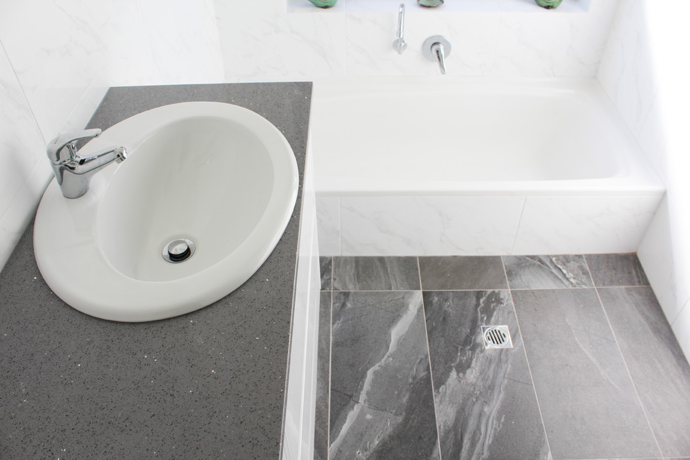 Modern inredning av ett litet grå grått badrum med dusch, med släta luckor, vita skåp, ett platsbyggt badkar, en dusch i en alkov, vit kakel, porslinskakel, vita väggar, klinkergolv i porslin, ett nedsänkt handfat, bänkskiva i kvarts, svart golv och dusch med gångjärnsdörr