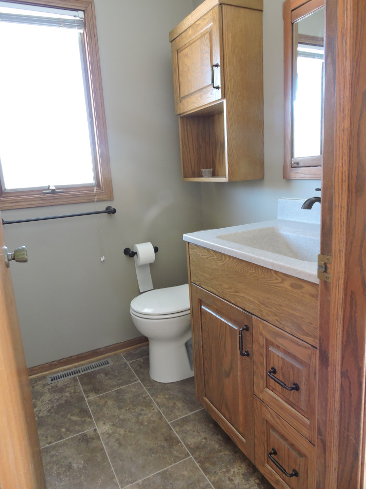 Photo of a small traditional bathroom in Other with raised-panel cabinets, medium wood cabinets, an alcove shower, a two-piece toilet, grey tiles, grey walls, vinyl flooring, an integrated sink, onyx worktops, brown floors, a hinged door, beige worktops and a single sink.