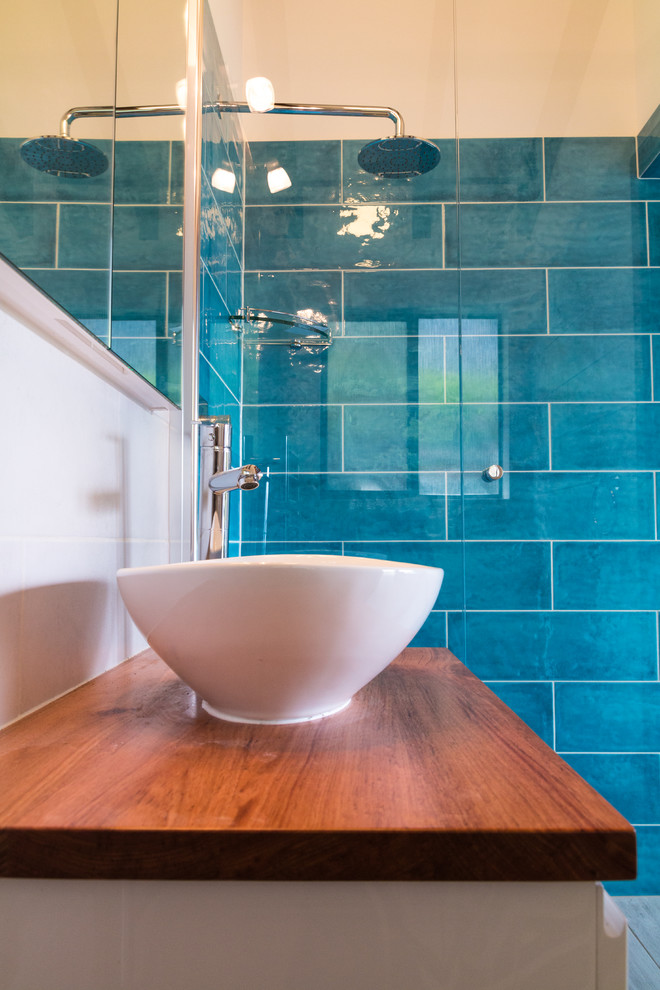 This is an example of a small contemporary shower room bathroom in Adelaide with freestanding cabinets, white cabinets, a corner shower, a one-piece toilet, ceramic tiles, blue walls, porcelain flooring, wooden worktops and blue tiles.