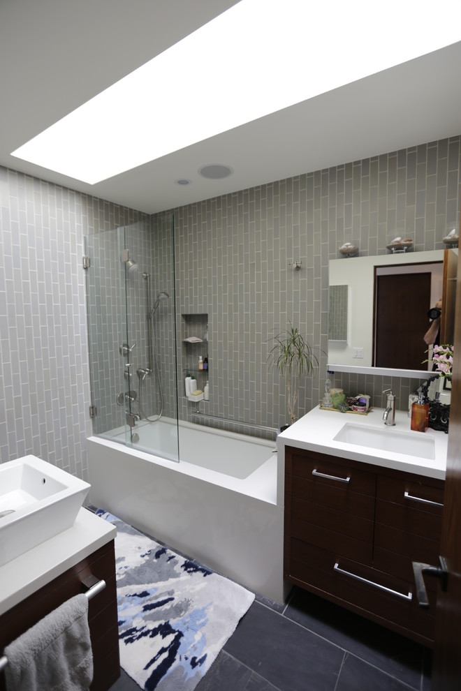 Cette image montre une petite salle de bain design en bois foncé avec une vasque, un placard avec porte à panneau encastré, un plan de toilette en bois, un combiné douche/baignoire, WC à poser, un carrelage gris, un mur beige et un sol en ardoise.