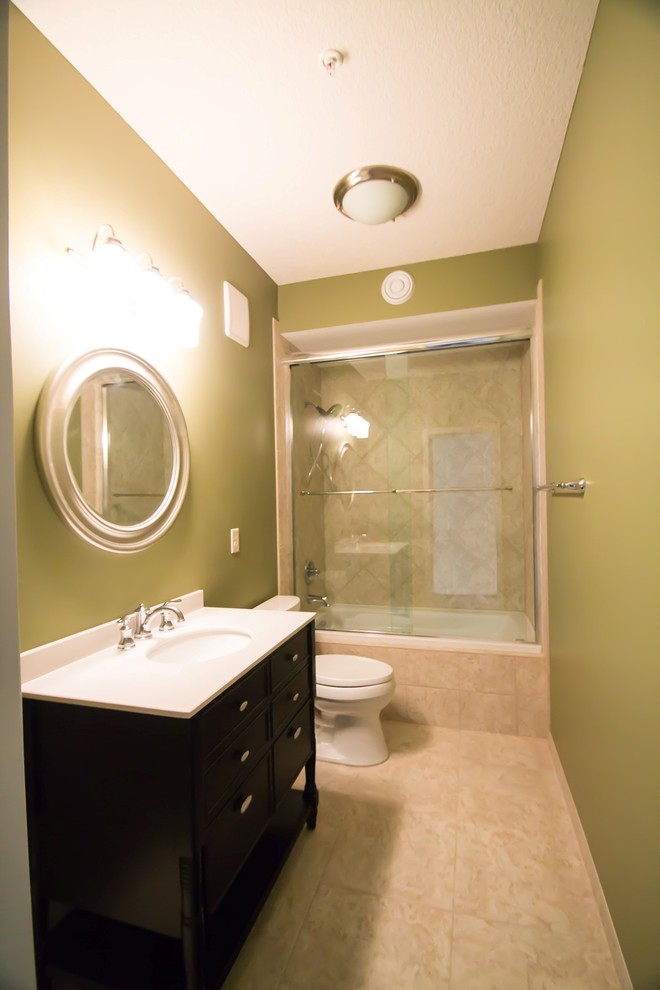 Bathroom - small traditional beige tile and stone tile travertine floor bathroom idea in Minneapolis with a console sink, furniture-like cabinets, black cabinets, solid surface countertops, a one-piece toilet and green walls
