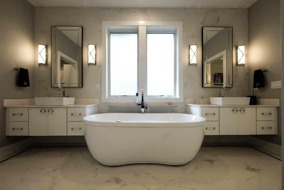 Large contemporary ensuite bathroom in Other with flat-panel cabinets, white cabinets, a freestanding bath, a two-piece toilet, grey tiles, white tiles, stone slabs, grey walls, marble flooring, a vessel sink and quartz worktops.
