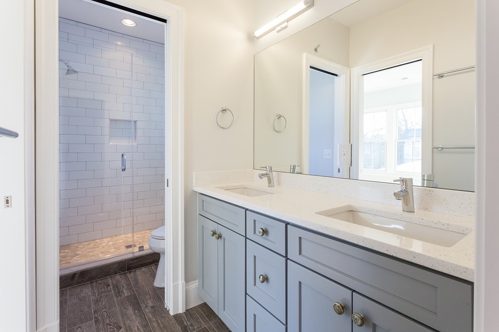 Photo of a farmhouse family bathroom in DC Metro with shaker cabinets, blue cabinets, an alcove shower, a two-piece toilet, white tiles, metro tiles, white walls, porcelain flooring, a submerged sink, engineered stone worktops, brown floors, a hinged door and white worktops.