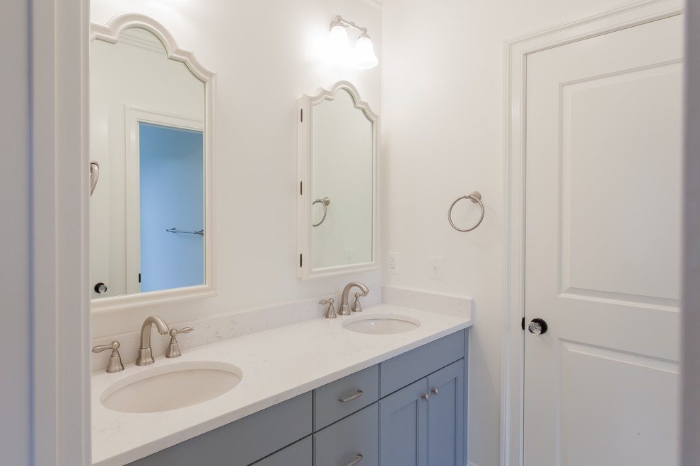 Modelo de cuarto de baño infantil de estilo de casa de campo con armarios estilo shaker, puertas de armario azules, baldosas y/o azulejos blancos, paredes blancas, lavabo bajoencimera y encimeras blancas