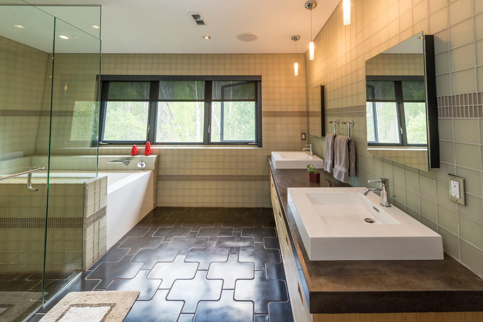 Design ideas for a large modern ensuite bathroom in Phoenix with a vessel sink, concrete worktops, flat-panel cabinets, light wood cabinets, an alcove bath, a corner shower, beige tiles, glass tiles, concrete flooring, black floors and a hinged door.