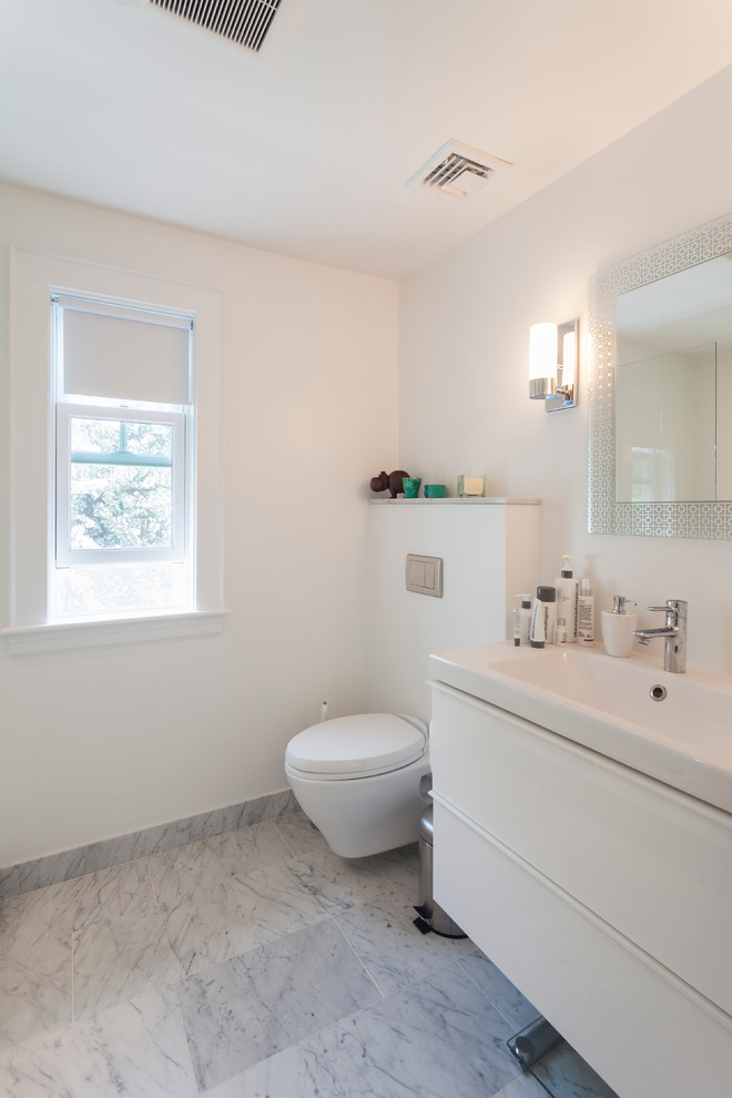 Diseño de cuarto de baño principal moderno de tamaño medio con lavabo integrado, armarios con paneles lisos, puertas de armario blancas, ducha empotrada, sanitario de pared, baldosas y/o azulejos de cerámica, paredes blancas y suelo de mármol