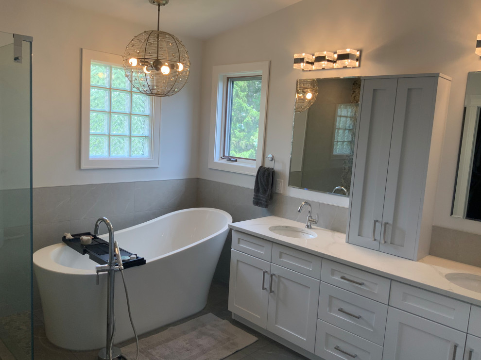 This is an example of a large traditional ensuite bathroom in Calgary with shaker cabinets, white cabinets, a freestanding bath, a corner shower, a two-piece toilet, grey tiles, porcelain tiles, grey walls, porcelain flooring, a submerged sink, engineered stone worktops, grey floors, a hinged door, white worktops, an enclosed toilet, double sinks, a built in vanity unit and a vaulted ceiling.