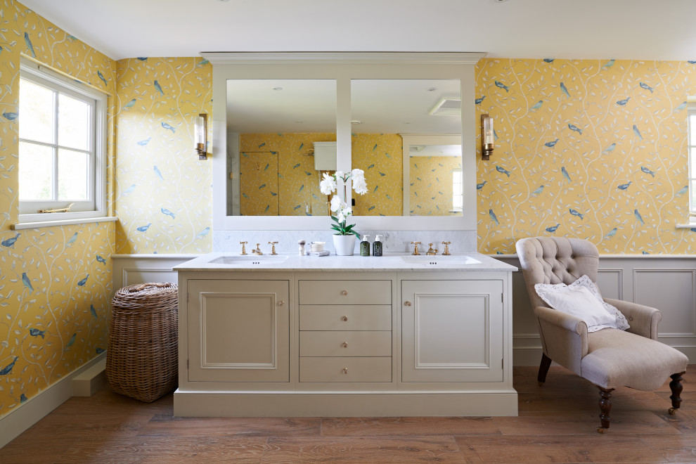 Foto på ett vintage vit badrum, med luckor med infälld panel, beige skåp, gula väggar, mellanmörkt trägolv, ett undermonterad handfat och brunt golv