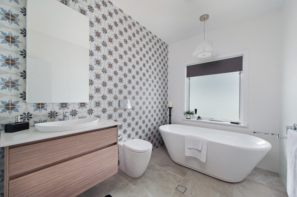Idée de décoration pour une salle de bain marine en bois clair de taille moyenne avec une vasque, un placard à porte plane, un plan de toilette en quartz modifié, une baignoire indépendante et un sol en travertin.